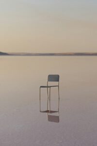 A lone chair sits in a shallow body of water.